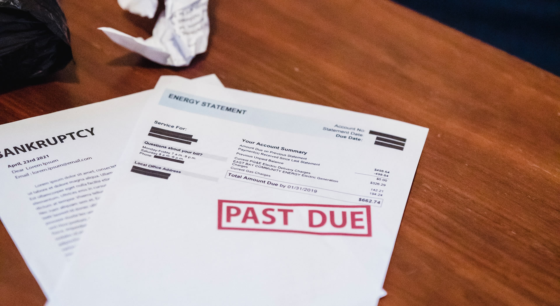 Bankruptcy letter and energy bill on a wooden table, with a red 'PAST DUE' stamp on the energy statement.
